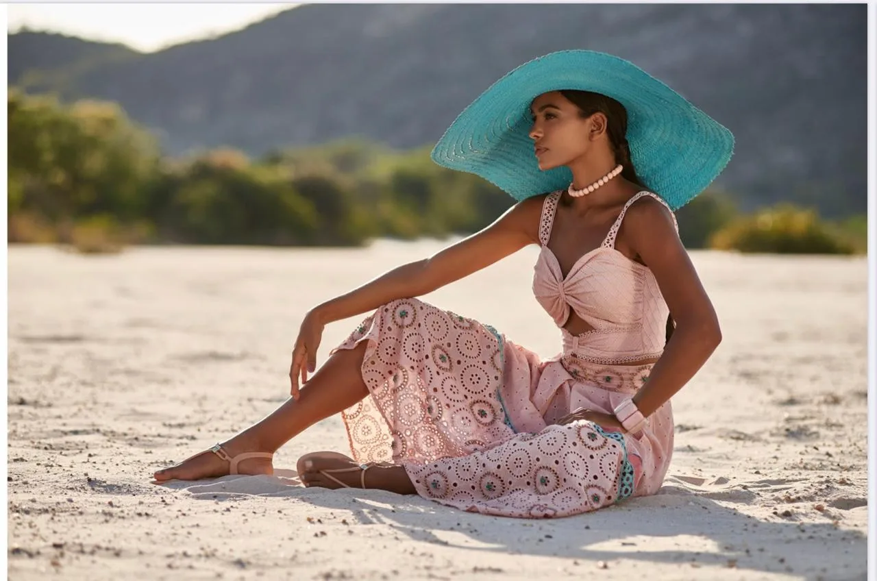 Anaiza Ferreira seated on sand wearing a turquoise wide-brim hat